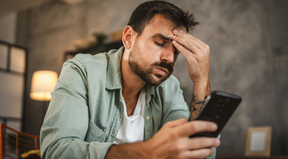 Ein Mann schaut genervt auf sein Smartphone und fasst sich an die Stirn.
