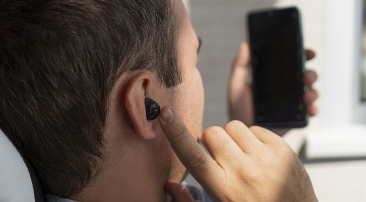 Ein Mann mit In-Ear-Kopfhörern im Ohr schaut auf sein Smartphone