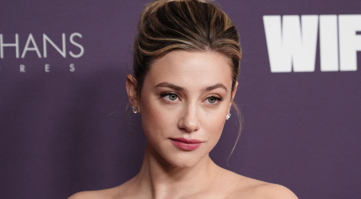 Auf dem Bild in dem Artikel zum The Love Hypothesis-Film ist Lili Reinhart vor einer violetten Pressewand zu sehen. Sie blickt leicht zur Seite