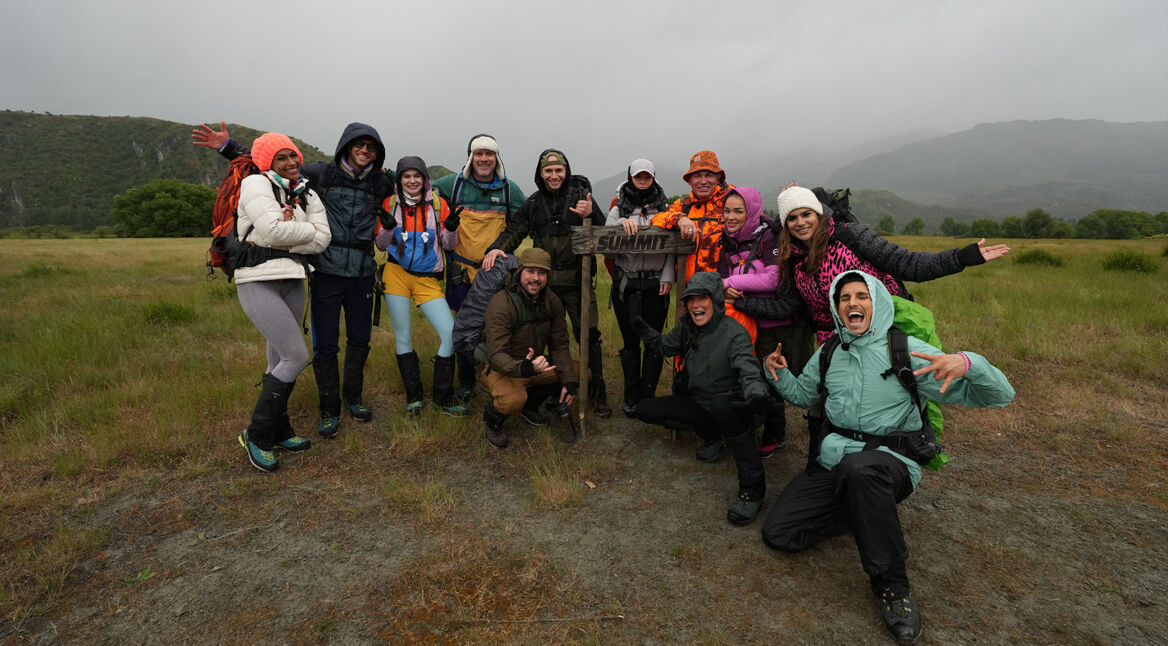 Auf dem Bild zur Reality-Show The Summit stehen die Teilnehmer*innen Cecilia Asoro, Flying Uwe, Klaudia Giez, Ansgar Brinkmann, Felix von Jascheroff, Serkan Yavuz, Julia Römmelt, Matthias Mangiapane, Giulia Siegel, Emmy Russ, Tanja Tischewitsch und PatroX lachend in einer Berglandschaft. Sie posieren stolz vor einem Schild mit der Aufschrift „Summit“ und wirken energiegeladen und siegessicher.