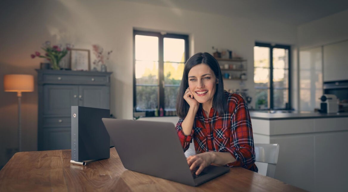 Router anschließen ohne Telefondose: Frau sitzt lächelnd vor einem Laptop.