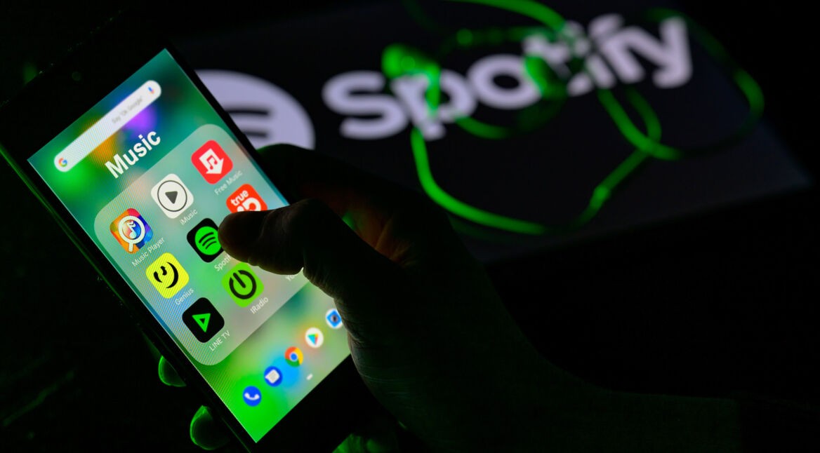Hand tippt auf das App-Symbol für Spotify auf einem Handy.