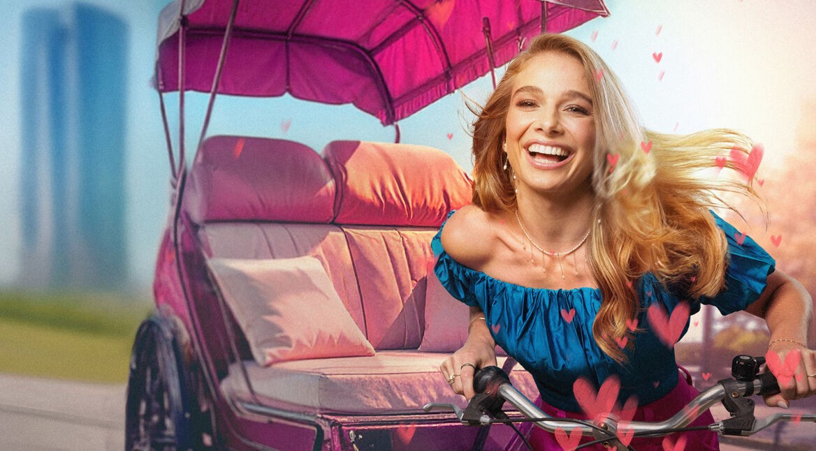 Auf dem Bild in dem Artikel zur ARD-Dating-Show City of Love sitzt Lola Weippert lachend auf einem pinken Fahrradtaxi. Sie trägt ein schulterfreies blaues Oberteil, während ihr blondes Haar zurückgeweht wird.