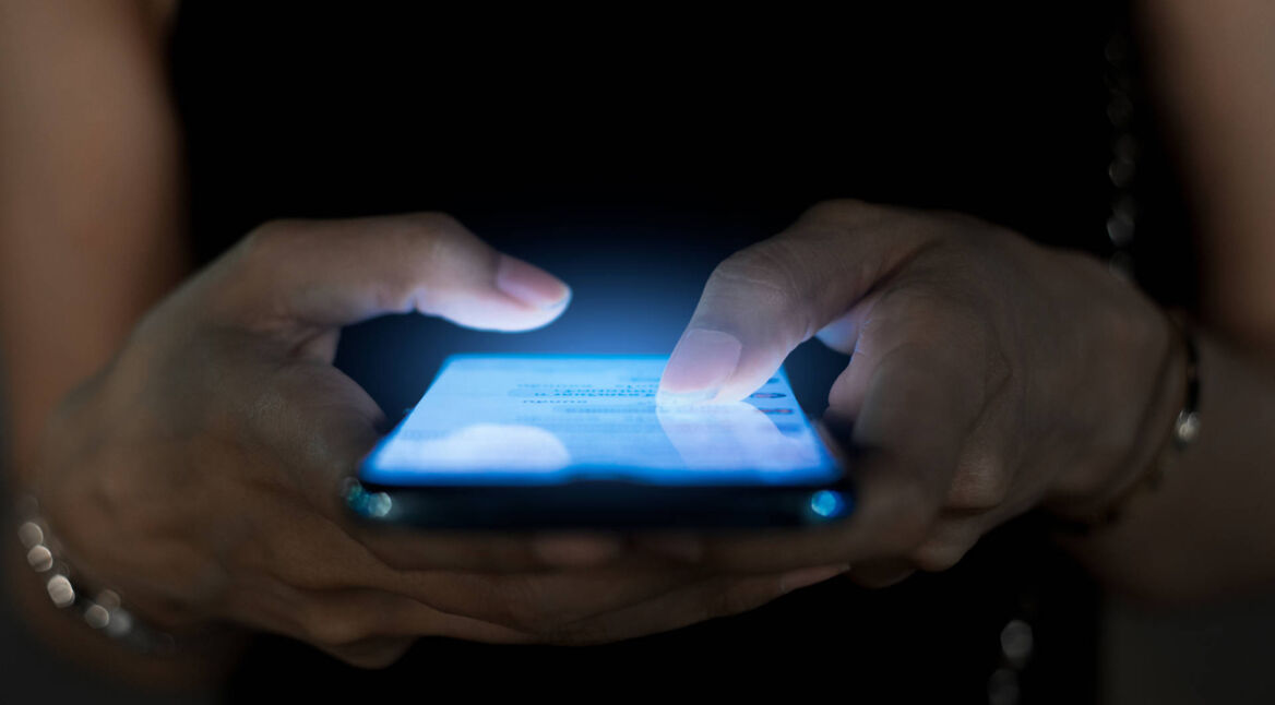 Nahaufnahme von zwei Händen, die in dunkler Umgebung auf einem Smartphone tippen.