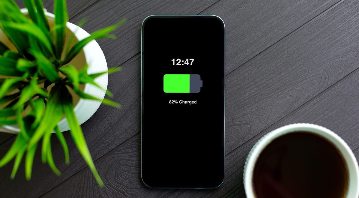 Im Artikel iphone-Akku tauschen zeigt dieses Bild ein modernes iPhone mit schwarzem Display auf einem dunklen Holztisch. Der Bildschirm zeigt 82 Prozent Akkuladung.