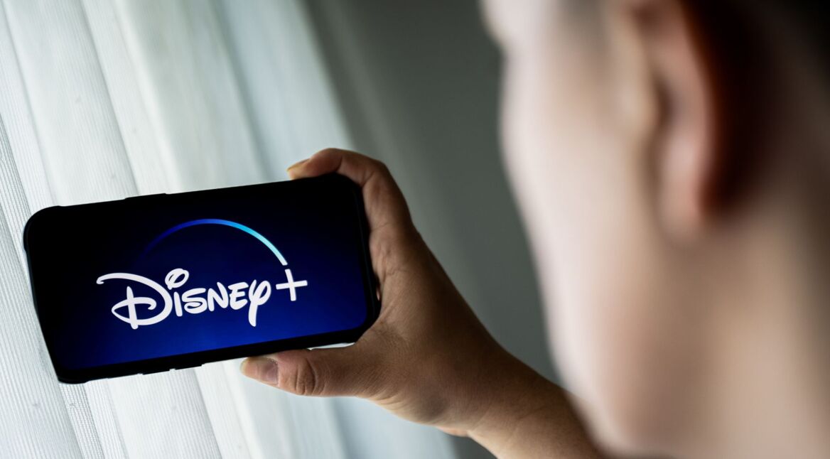 Mann schaut auf sein Smartphone, das das Logo von Disney+ zeigt.