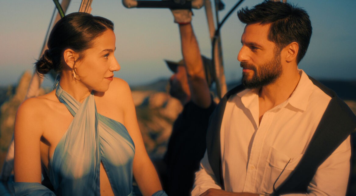 Szenenbild aus dem Netflix-Film She Said Maybe: Eine elegant gekleidete Frau und ein gut aussehender Mann mit Bart blicken sich an.