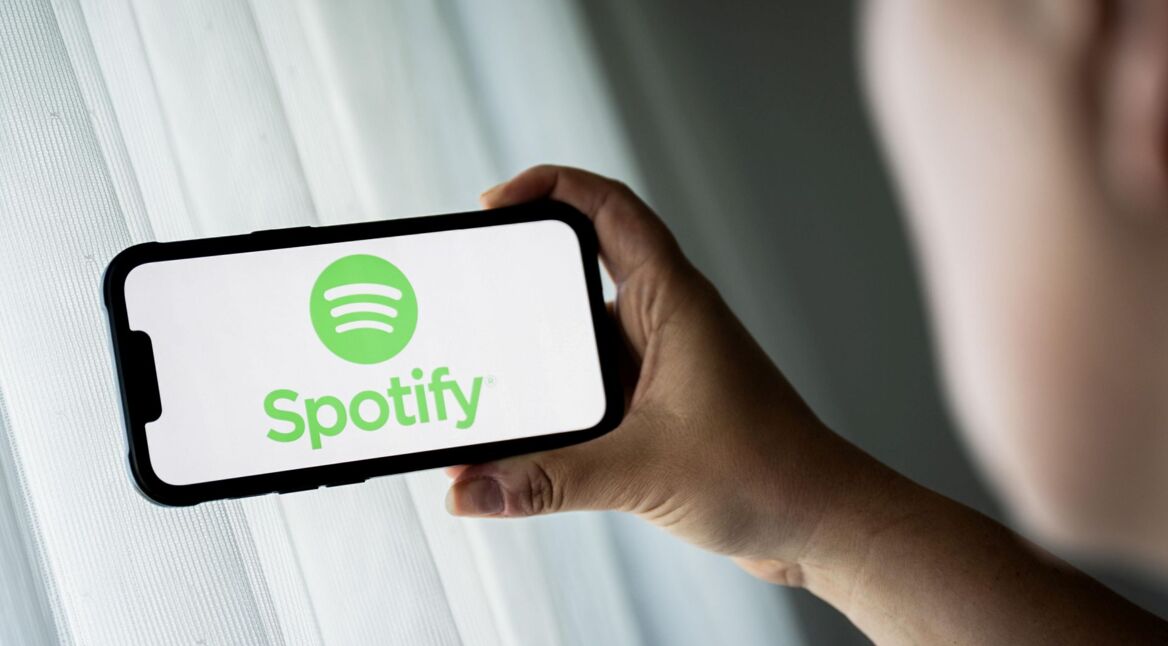 Mann schaut auf iPhone-Display, auf dem das Logo von Spotify abgebildet ist.