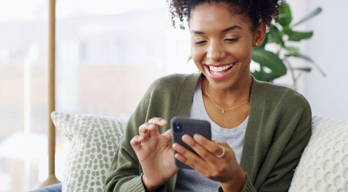 Junge Schwarze Frau schaut lächelnd auf ihr Android-Handy.