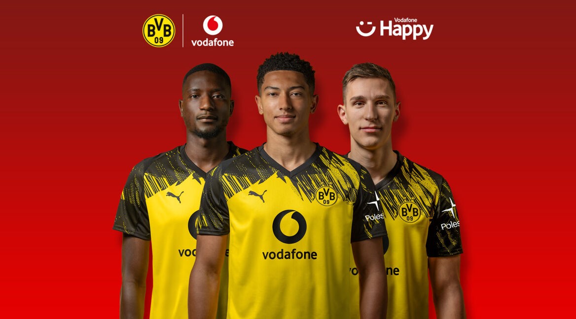 Auf dem Bild in dem Artikel zum BVB-Gewinnspiel stehen drei Spieler von Borussia Dortmund nebeneinander vor einem roten Hintergrund. Sie tragen das gelb-schwarze Trikot mit dem Vodafone-Logo auf der Brust. Über ihnen sind die Logos von BVB, Vodafone und Vodafone Happy zu sehen.