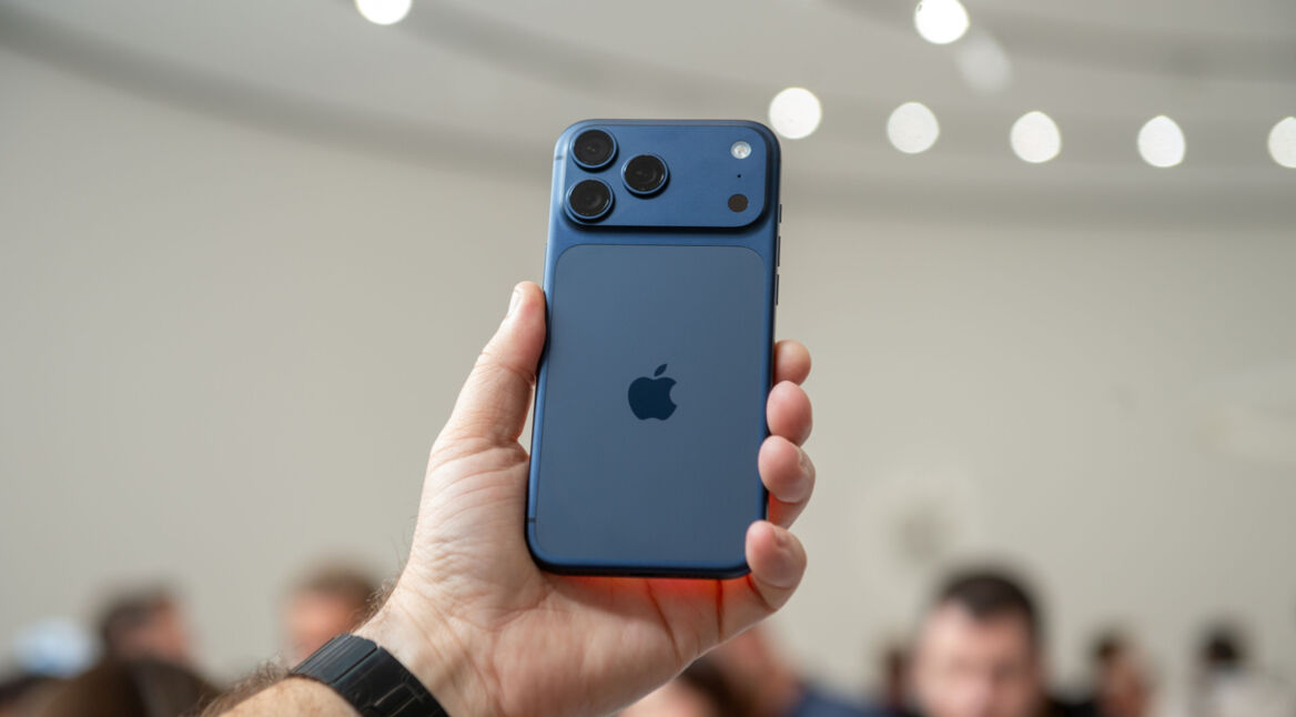 Hand hält das iPhone 17 Pro in Blau in die Höhe, im Hintergrund sind unscharf Menschen zu erkennen