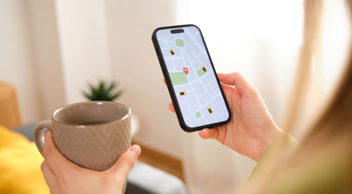 Frau mit Tasse in der Hand schaut auf die Navigations-App auf ihrem iPhone.