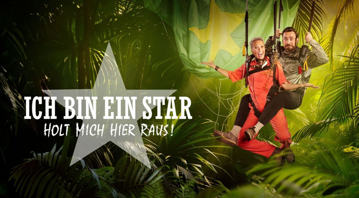 Promofoto zum Dschungelcamp 2026. Die beiden Moderator:innen Sonja Zietlow und Jan Köppen hängen in Fallschirmen vor einer Dschungelkulisse.