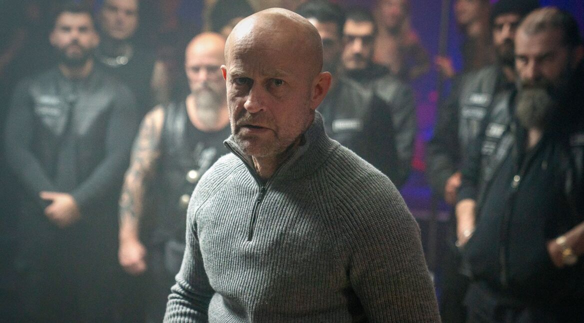 Jürgen Vogels Robert steht mit dem Rücken vor den Männern eines Motorradclubs.