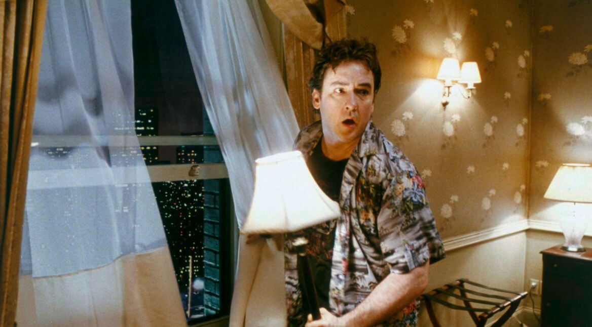 Filmszene aus Zimmer 1408: Mike Enslin (John Cusack) steht mit einer Lampe in der Hand vor dem geöffneten Fenster und schaut sich ängstlich um.