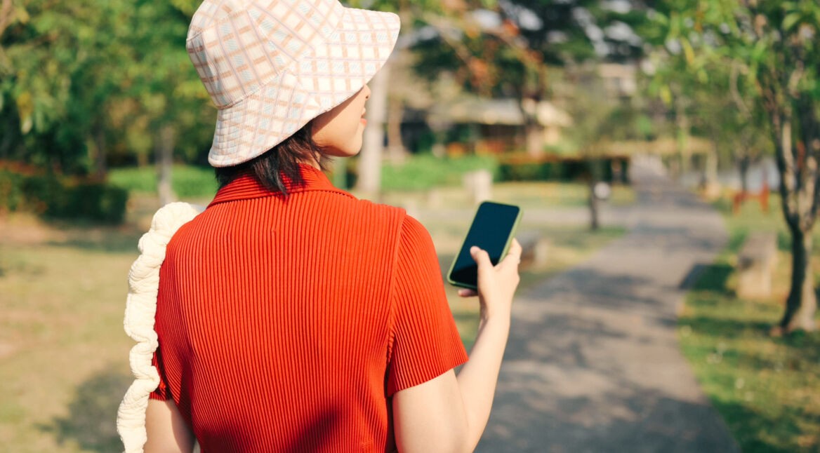 Eine Frau geht spazieren und hält dabei ihr Smartphone in der Hand.