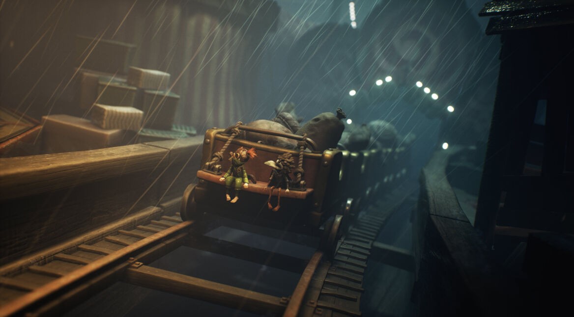 In der Szene aus dem Little Nightmares 3-Tipps-Artikel sitzen Low und Alone in einem offenen Minenwagen, der bei starkem Regen über wackelige Schienen rollt.