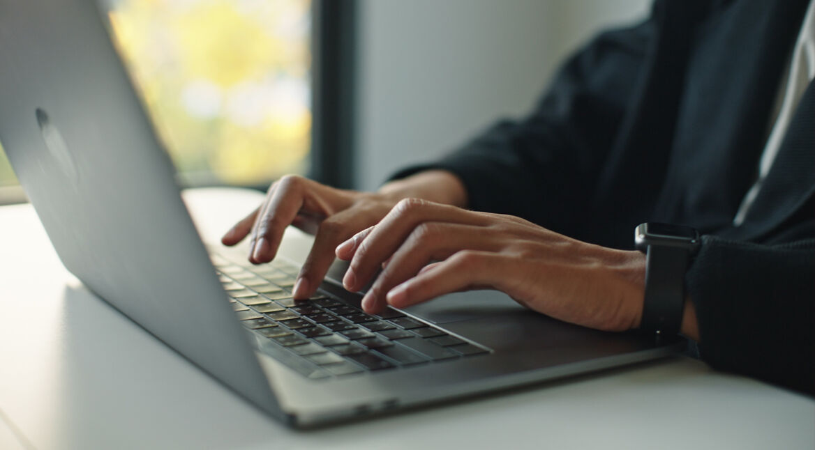 Auf dem Bild mit symbolischem Bezug zu Perplexity Pro ist eine Person in Business-Kleidung zu sehen, die konzentriert auf einem modernen Laptop tippt. Die Szene wirkt professionell und fokussiert, im Hintergrund ist ein Fenster mit natürlichem Licht und unscharfem Ausblick zu erkennen. Am Handgelenk trägt die Person eine Smartwatch.