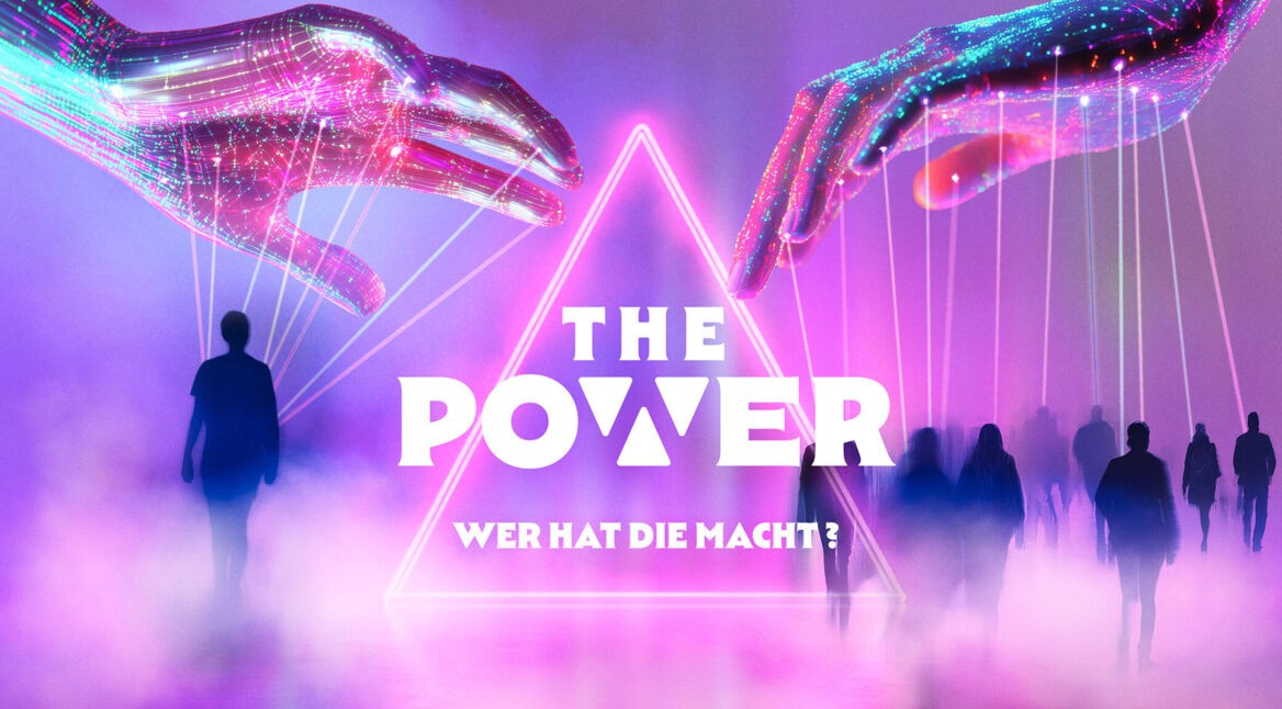 Auf dem offiziellen Visual zu "The Power" von Joyn schweben zwei leuchtende, digitale Hände über einer Gruppe von Menschen, die im Nebel auf eine neonbeleuchtete Pyramide zulaufen. Die Hände steuern die Figuren wie Marionetten. Die Farben sind dominiert von Violett, Pink und Blau, was eine mysteriöse und futuristische Stimmung erzeugt.