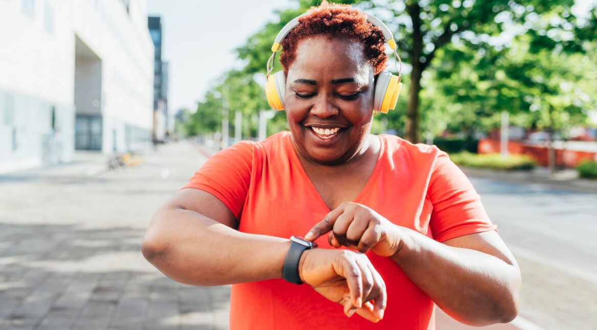 Eine Frau mit Kopfhörern bedient lächelnd ihre Apple Watch