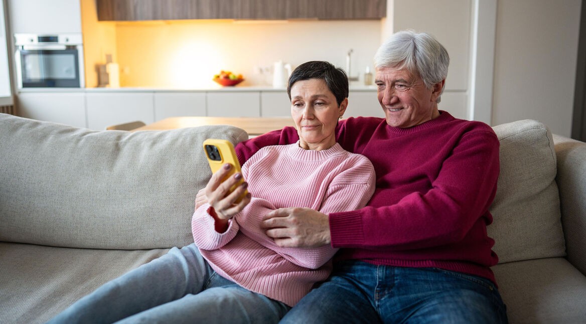 Ein älteres Pärchen sitzt auf dem Sofa und schaut auf ein Smartphone.