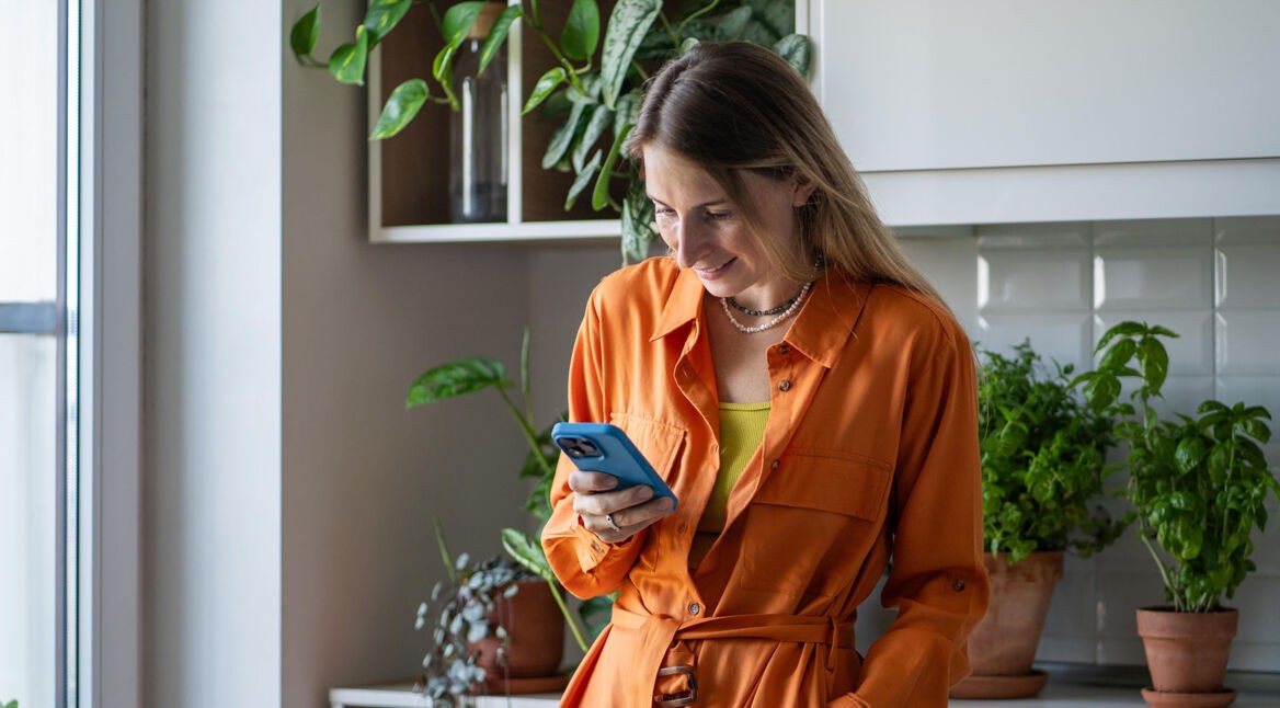 Eine Frau lehnt an einem Schrank und schaut auf ein Smartphone.
