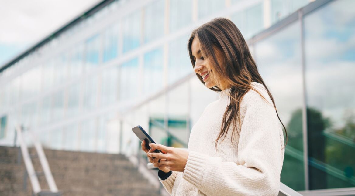 Junge Frau schaut auf ein Handy, das sie in den Händen hält.