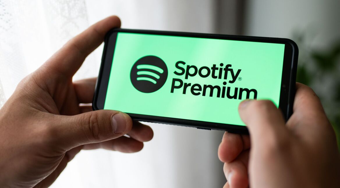 Das Spotify-Logo und der Text "Spotify Premium" sind auf einem Handy zu sehen, das jemand in der Hand hält.