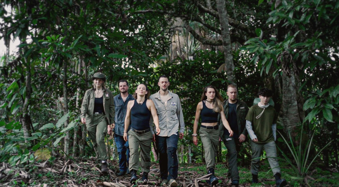 Auf dem Bild zu 7 vs. Wild Gewinner:innen sind sieben Teilnehmende im Dschungel zu sehen. Von links nach rechts: Jeannine Michaelsen, Joe Vogel, Fibii, Lucas „Avive“ Michels, Imke Salander, Kris Grippo und David Leichtle. Alle tragen Outdoor-Kleidung und wirken fokussiert und entschlossen, während sie durch dichtes Grün marschieren.