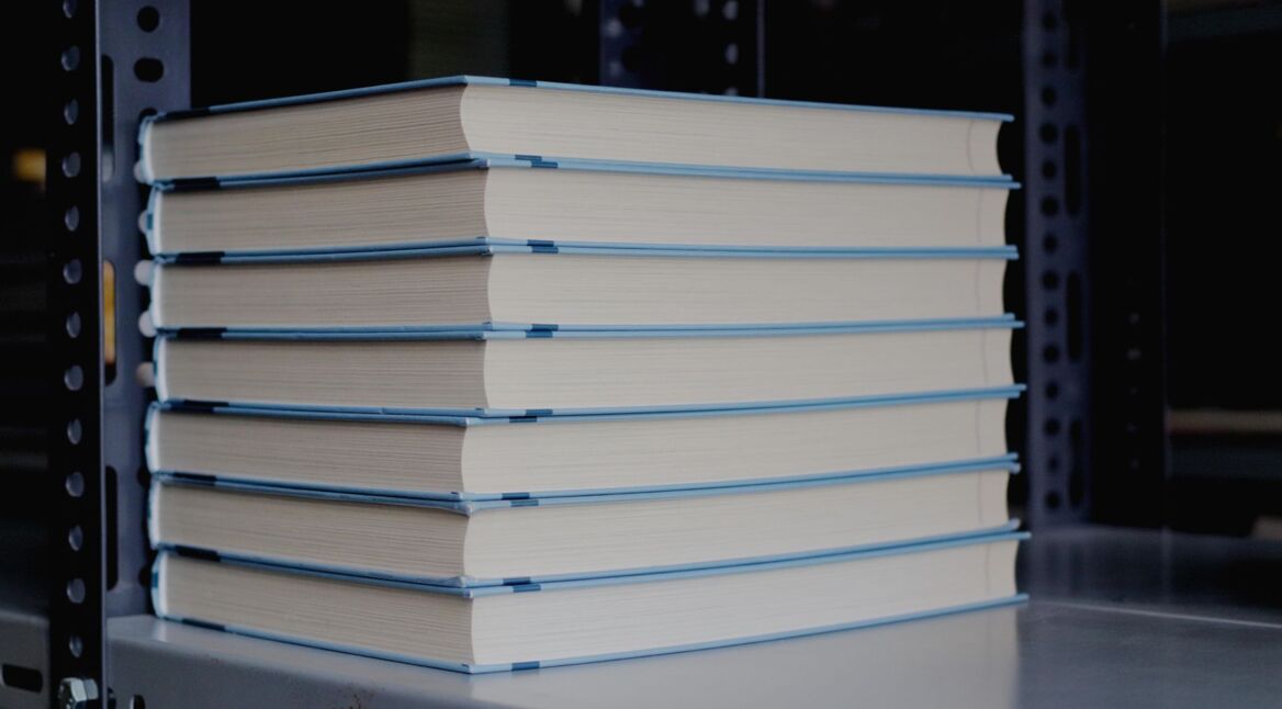 Bücher stehen gestapelt in einem Regal.