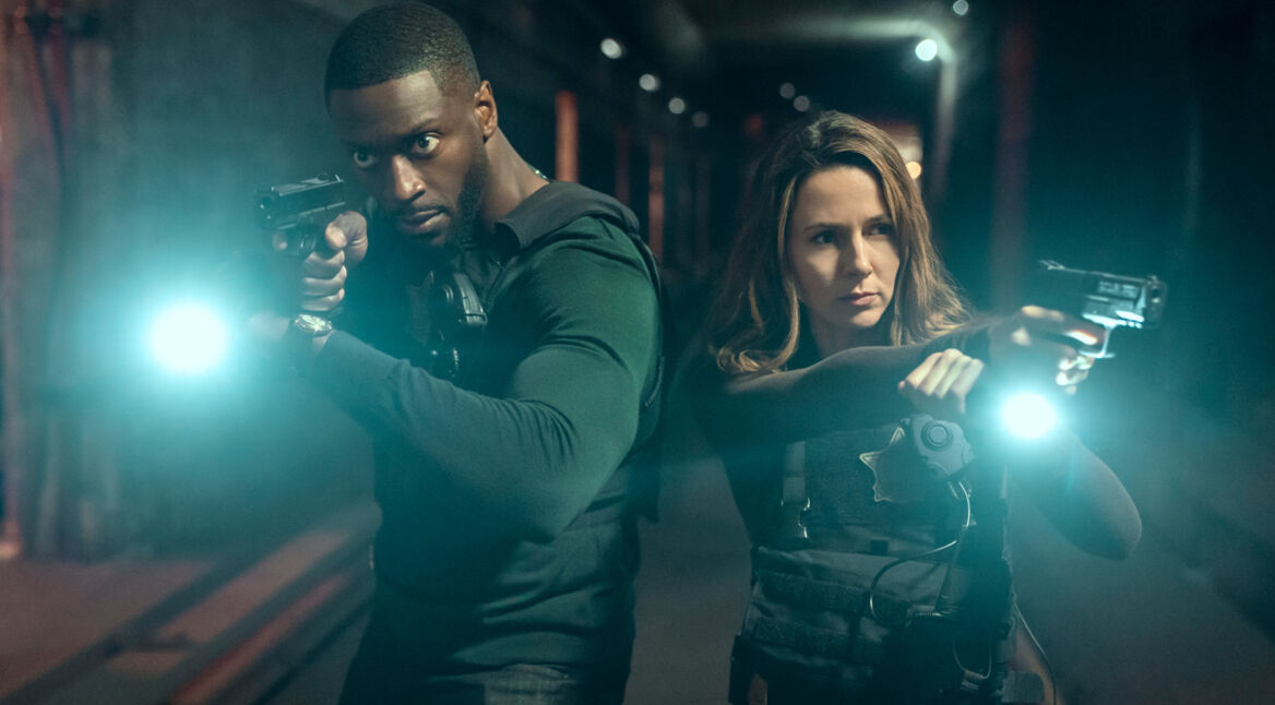 Aldis Hodge als Detective Alex Cross und Alona Tal als Special Agent Kayla Craig. Beide stehen mit gezogener Pistole und einer Taschenlampe im Dunkeln.