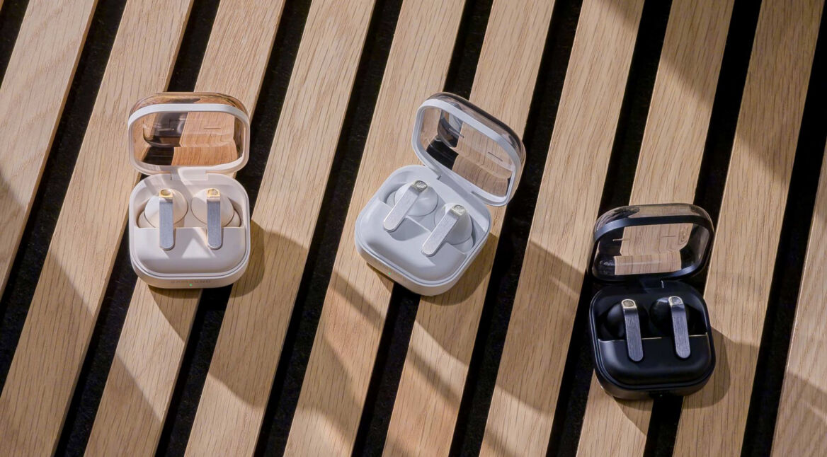 Drei Ausführungen der Kopfhörer Galaxy Buds4 Pro im Ladecase liegen auf einem Holztisch.