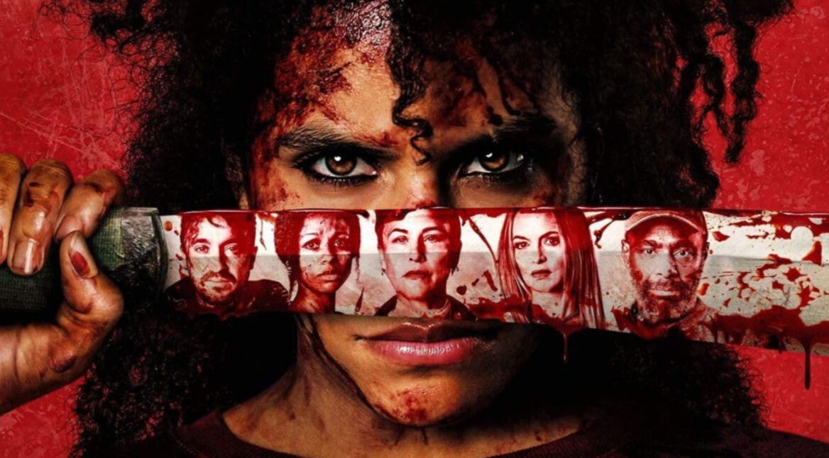 Zazie Beetz in They Will Kill You: Eine blutverschmierte Frau mit intensivem Blick hält sich eine Machete vors Gesicht auf der mehrere Gesichter zu sehen sind.