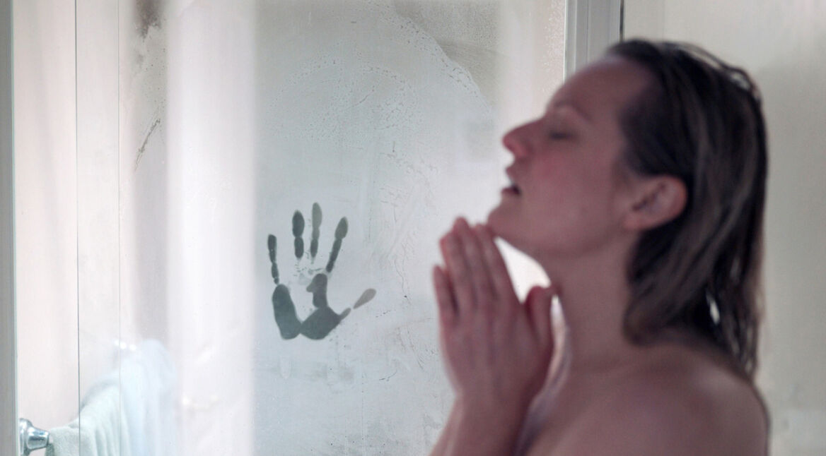 Cecilia (Elisabeth Moss) steht mit geschlossenen Augen unter der Dusche. An der Glaswand der Dusche hat der Unsichtbare einen Handabruck hinterlassen.