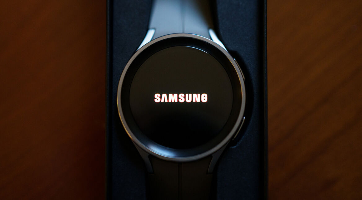 Auf dem Bild zu Samsung Galaxy Watch Modelle ist eine moderne Samsung Smartwatch in einer eleganten Nahaufnahme zu sehen. Die Uhr liegt in einer Verpackung und zeigt auf dem runden Display das leuchtende Samsung-Logo. Das Gehäuse wirkt hochwertig und minimalistisch, während das dunkle Armband dezent im Hintergrund verschwindet. Die Stimmung ist edel, technisch und hochwertig inszeniert.
