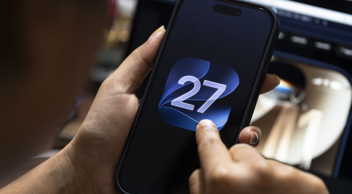 Eine Person interagiert mit einem iPhone, auf dessen Display das Logo von iOS 27 zu sehen ist.