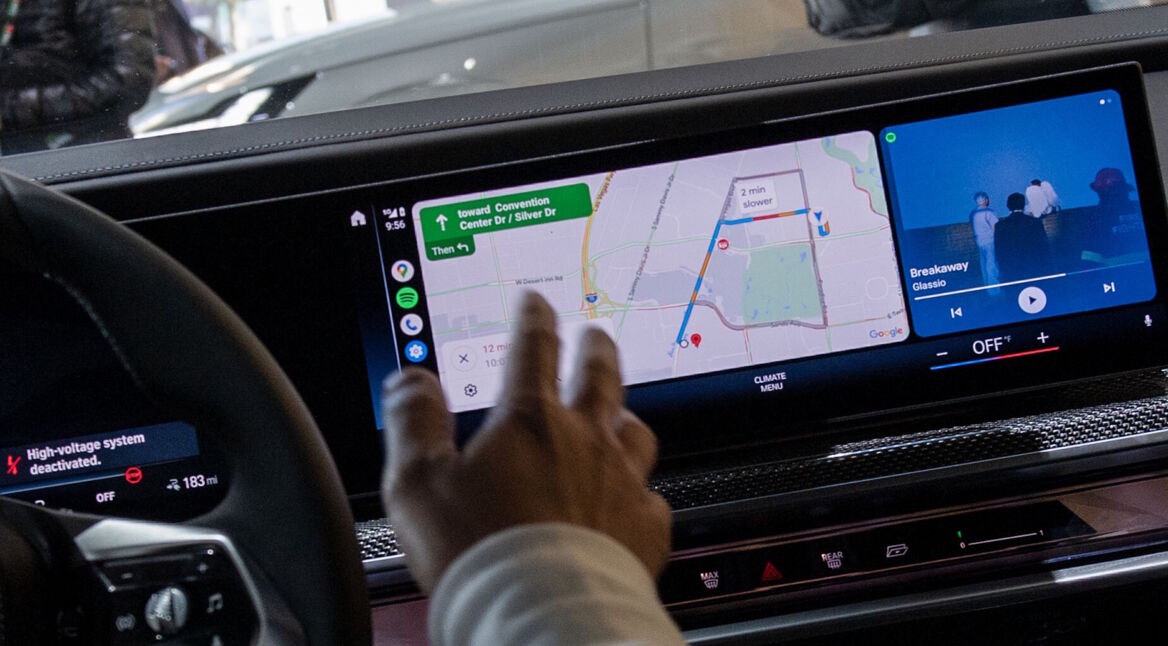 Ein Googles-Mitarbeiter sitzt am Steuer eines Autos und stellt Android Auto vor.