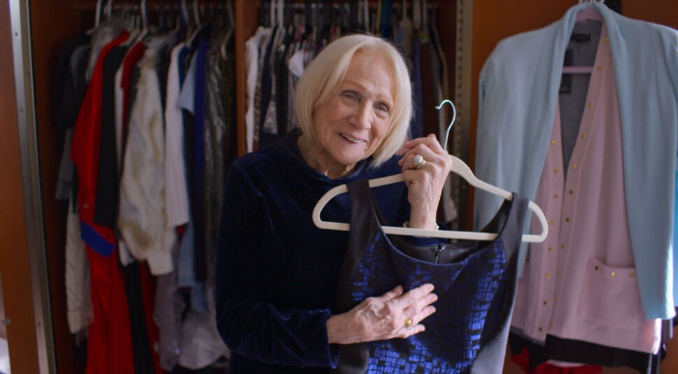 Eine Frau steht vor ihrem Kleiderschrank und hält ein Kleid in den Händen.