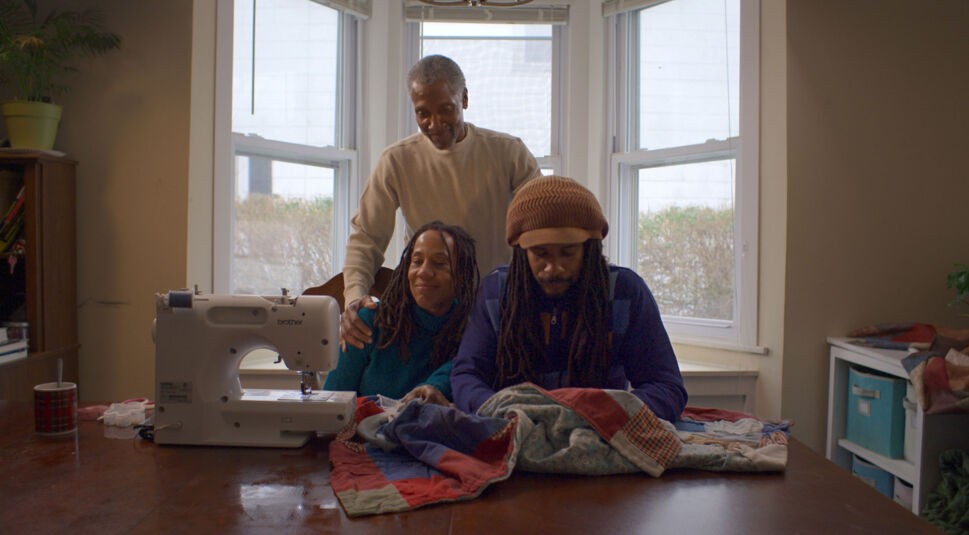 Drei Personen sitzen an einem Tisch auf dem eine Nähmaschine steht