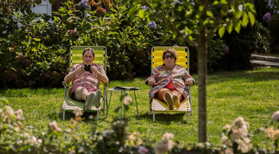 Die Nachbarn Mitch und Mo liegen im Garten und schauen durch ein Fernglas.