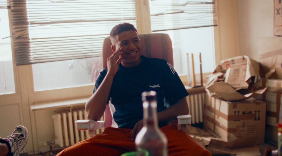 Sanchez (Aaron Maldonado-Morales) sitzt unbeschwert in seiner Wohnung im dem Film Sonne und Beton