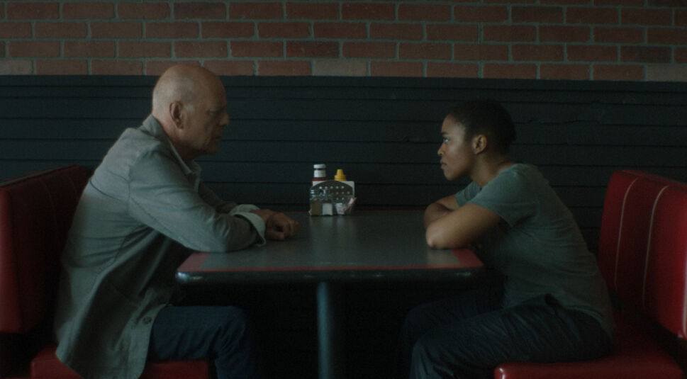 Bruce Willis als Valmora sitzt Nomzamo Mbath als Alexa an einem Tisch in einem Dinner gegenüber in Bruce Willis’ letztem Film Assassin – Every Body is a Weapon