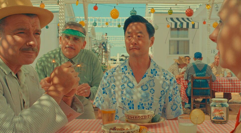 Personen sitzen in Asteroid City am Tisch und schauen sich an.