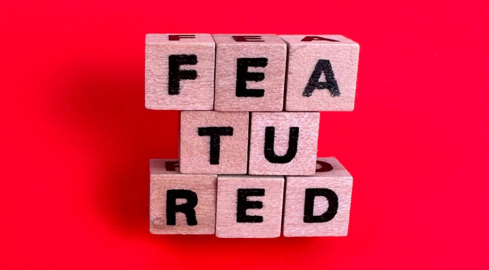 Buchstabenwürfel aus Holz formen vor rotem Hintergrund das Wort featured