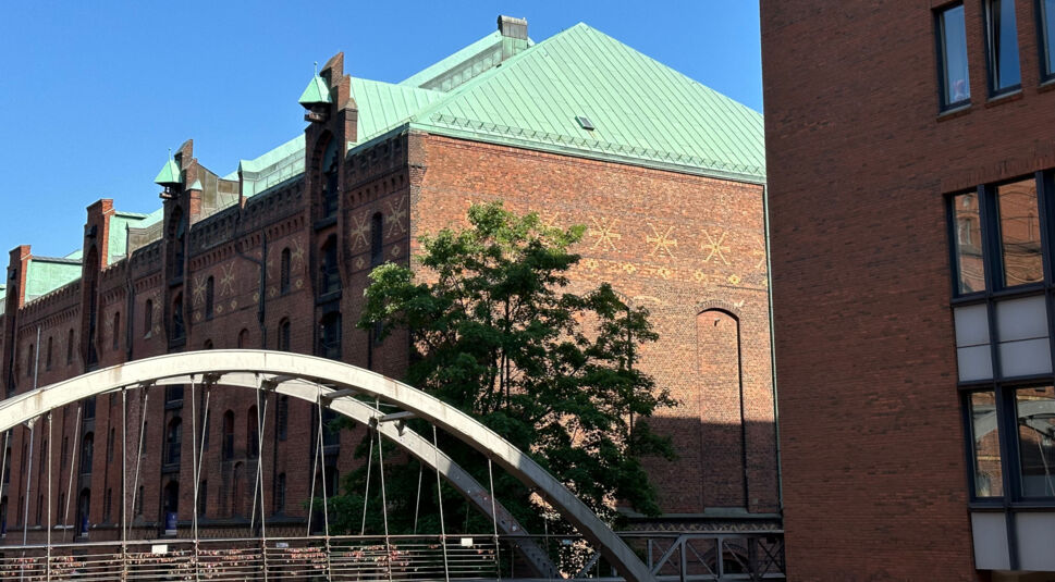 Träger eines Eisenbrücke neben rotem Backsteinhaus mit grünem Dach