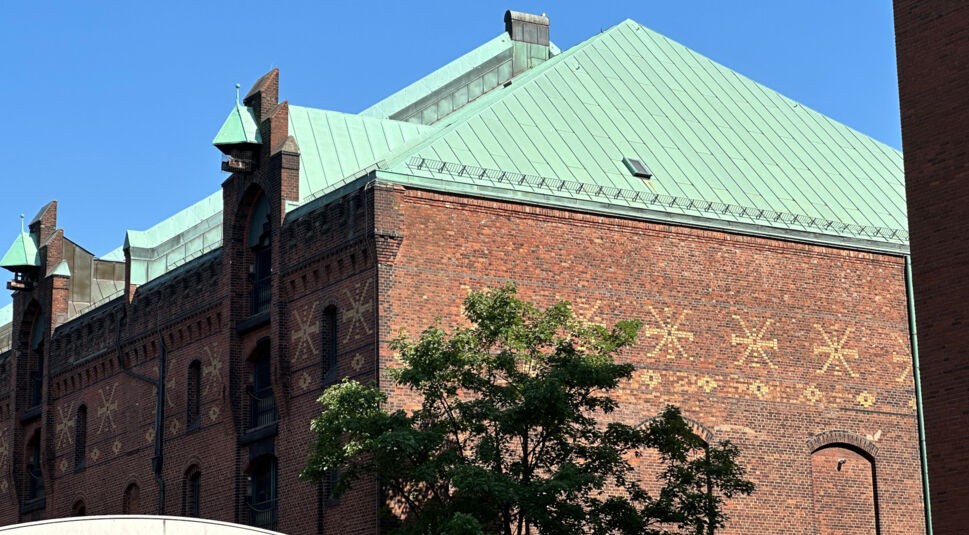 Träger eines Eisenbrücke neben rotem Backsteinhaus mit grünem Dach