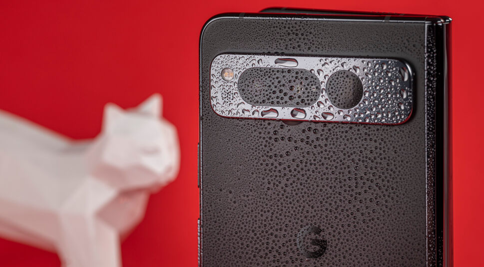 Smartphone Google Pixel Fold von außen mit Wassertropfen auf der Hülle vor rotem Hintergrund