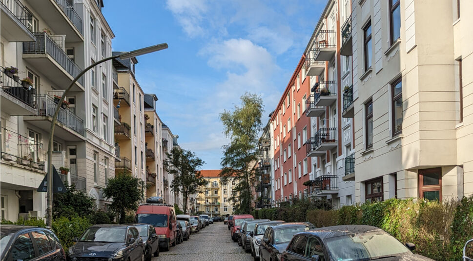 Enge Straße mit Kopfsteinpflaster und Autos auf beiden Seiten, gelbes Haus am Ende