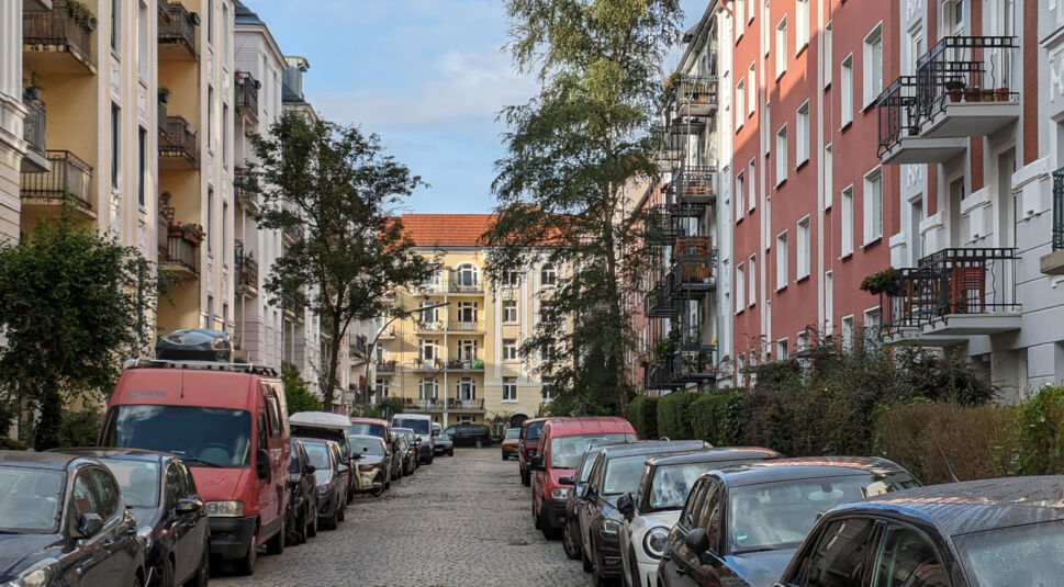Enge Straße mit Kopfsteinpflaster und Autos auf beiden Seiten, gelbes Haus am Ende
