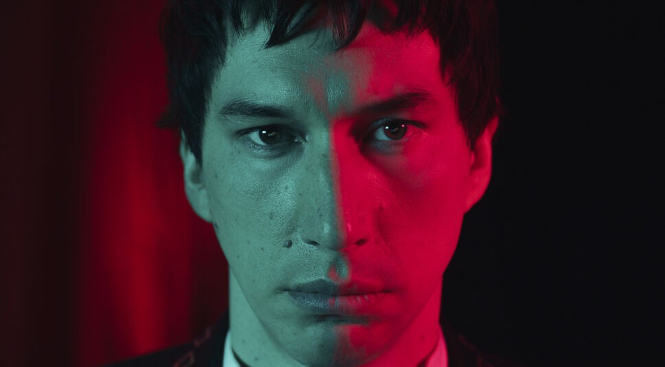 Auf dem Bild aus dem Film "Megalopolis" ist Adam Driver in einer Nahaufnahme zu sehen. Die linke Hälfte seines Gesichts ist in kühlem Blau und die rechte Hälfte in intensivem Rot beleuchtet, was eine düstere und geheimnisvolle Stimmung erzeugt. Sein Blick ist ernst und durchdringend, während der Hintergrund dunkel bleibt, um den Fokus auf sein Gesicht zu lenken.